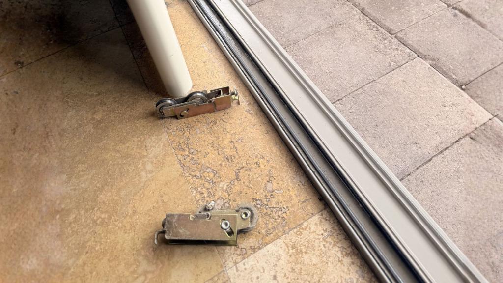 Worn sliding door rollers removed and placed beside track during repair and replacement process