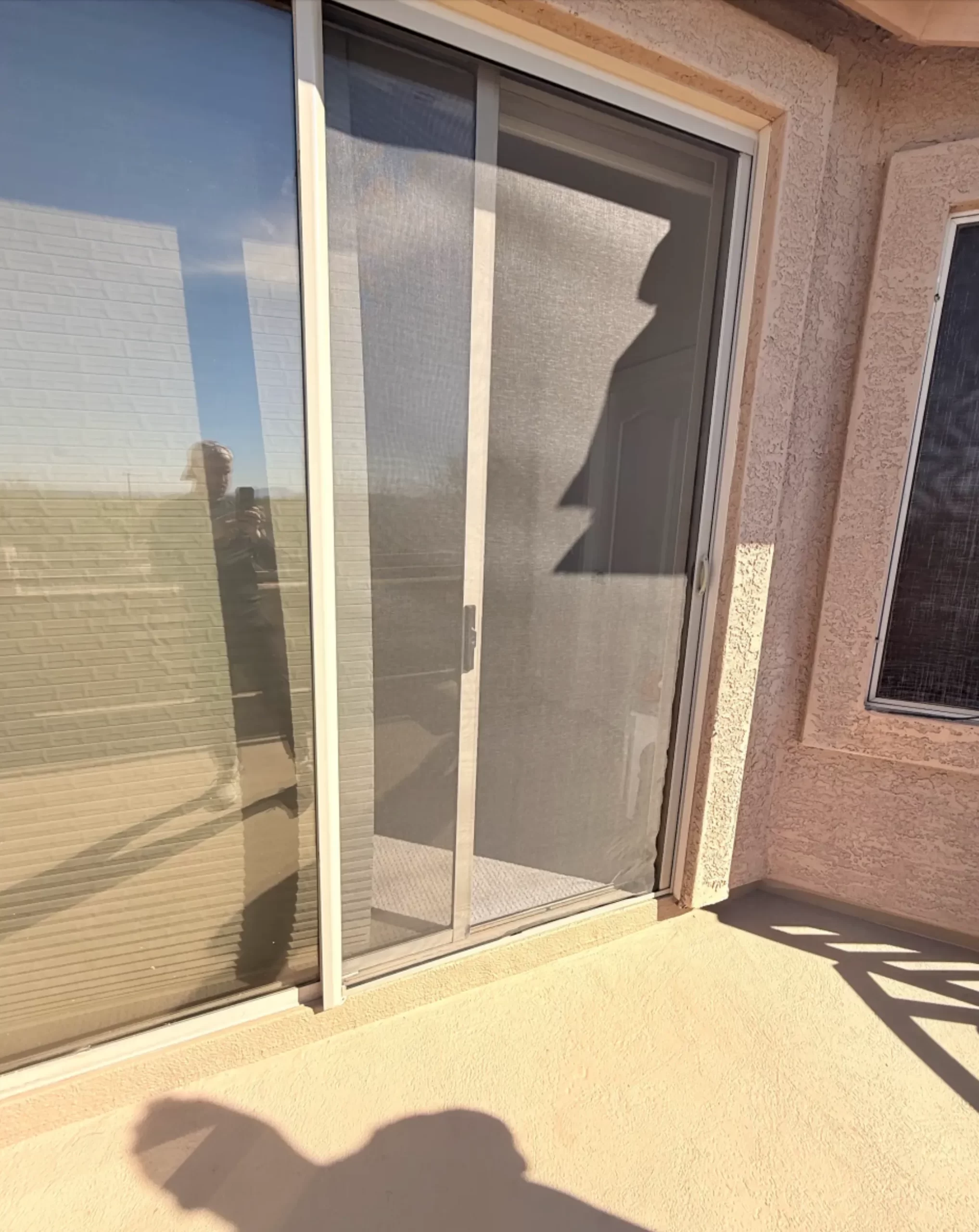 Sliding glass door with screen and reflection of person on a sunny day