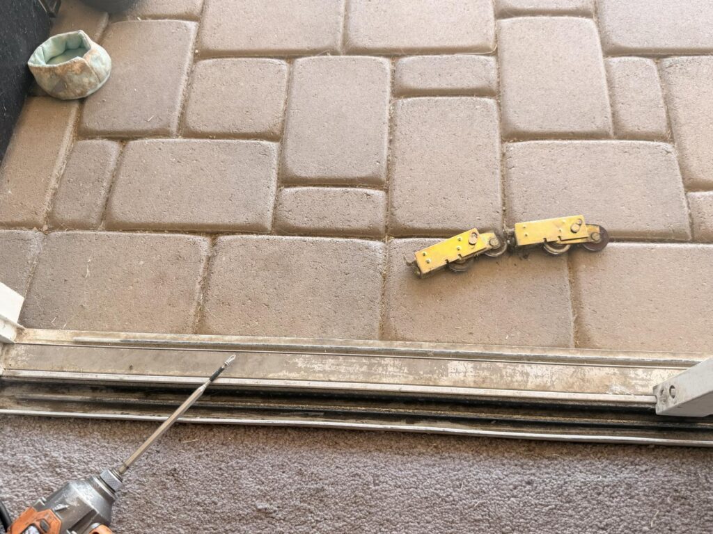 Two yellow sliding door rollers and a screwdriver on a patio.