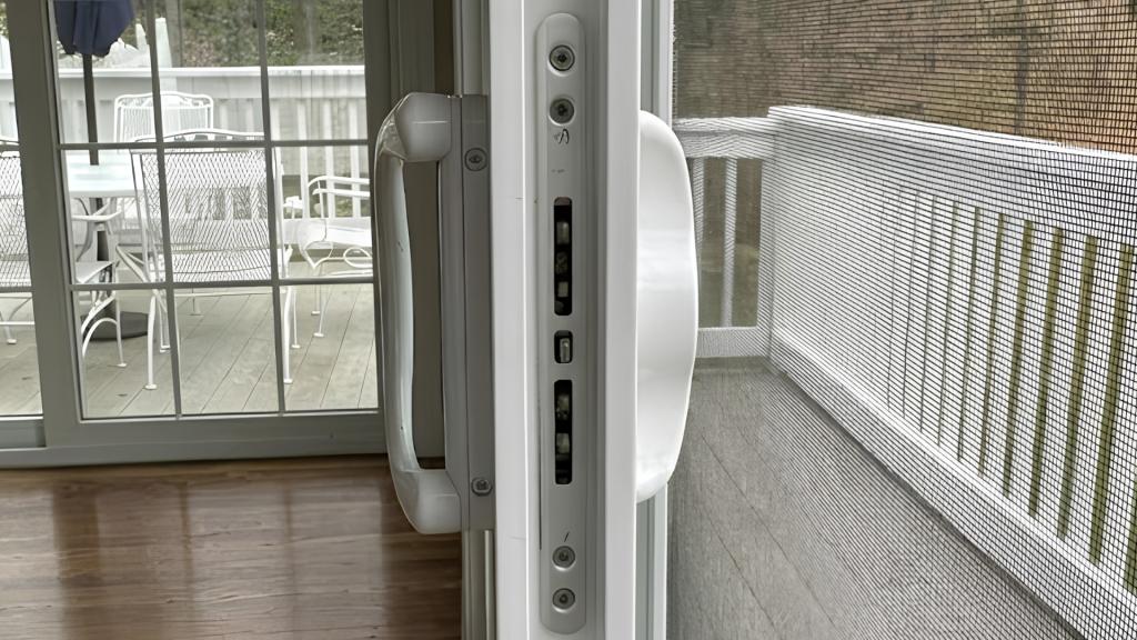 Close-up of a white sliding glass door handle and lock hardware near a patio screen, used for a guide about why a sliding door won’t lock