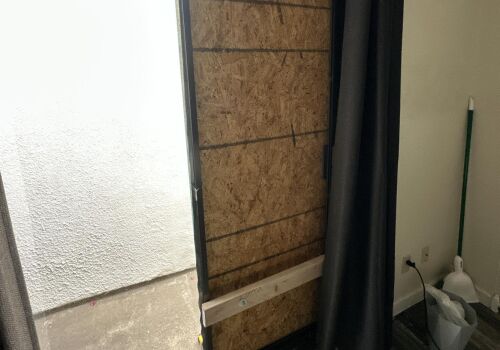Sliding glass door boarded up with plywood from the inside of a room