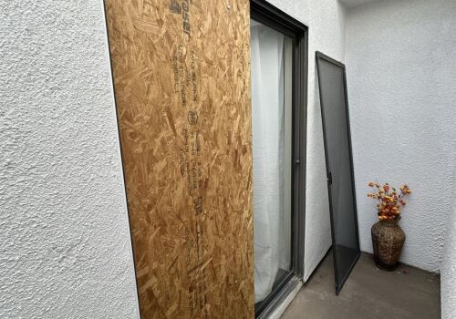 Boarded-up sliding glass door with a screen leaning against a wall.