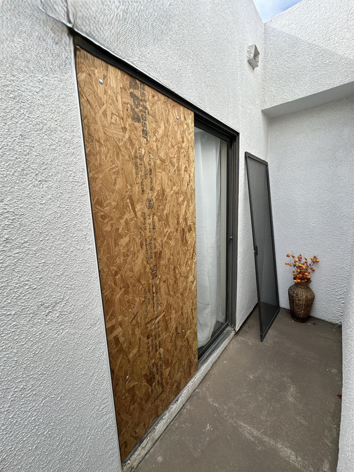 Boarded-Up Sliding Glass Door on a White Stucco Building Boarded-up sliding glass door with a screen leaning against a wall.