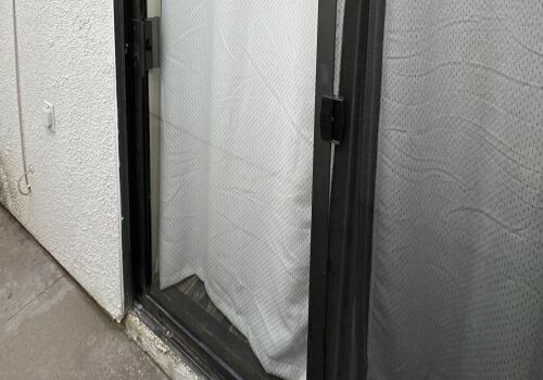 Close-up of a glass sliding door with white curtains and a screen door.