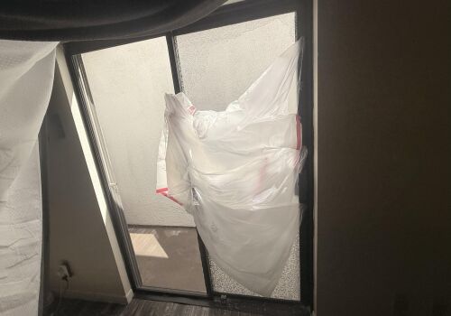 Plastic bags taped over a broken glass door, with sunlight shining through.